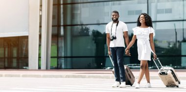 Gülümseyen siyah bir çift havaalanı binasının önünde birlikte yürür, bagajlarını arkalarından çekerler. İkisi de dört gözle bekliyor ve birlikte iyi vakit geçiriyor gibi görünüyorlar..