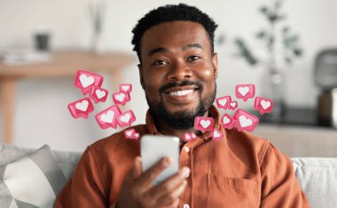 Genç bir Afro-Amerikan adam koltuğunda oturuyor, telefonuna bakarken gülümsüyor. Çevresi dijital kalp simgeleriyle çevrili, sosyal medyada beğeni ve olumlu katılımı temsil ediyor..