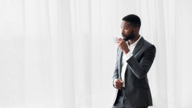 Ciddi Afro-Amerikan iş adamı iş yerinde yoğun bir günün ardından ofis penceresinin yanında kahve içiyor.