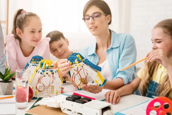Bir grup genç öğrenci bir sınıf ortamında robotik ve mühendislik öğreniyor. Bir öğretmen birlikte çalışıp sorular sorarken bir robot yapıp programlamalarına yardım ediyor..