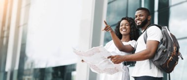 African American couple, dressed casually in white shirts, smiles and points towards a direction while holding a map, copy space clipart