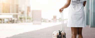 Kameradan bir parça bavulla ayrılan bir kadın. Açık renkli bir elbise giyiyor ve şehir ortamında fotokopi çekiyor.