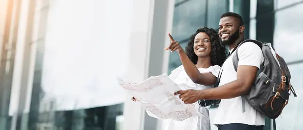 stock image African American couple, dressed casually in white shirts, smiles and points towards a direction while holding a map, copy space