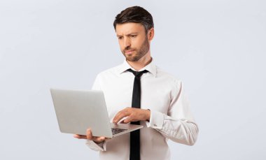 Beyaz gömlekli ve siyah kravatlı bir işadamı dizüstü bilgisayarı üzerinde çalışıyor. Klavyede yazarken endişeli görünüyor..