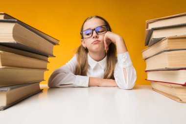 Sıkıcı dersler. Üzgün İlköğretim Okulu Kız Sarı Arka Plan Üzerinde İki Kitap Yığınları Arasında Oturan. Stüdyo Çekimi