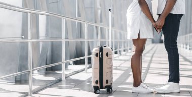 Bir havaalanı terminalinde el ele tutuşan çift birbirine yakın duruyor. Büyük bir pencerenin önünde duruyorlar, gümüş korkuluklu, kopyalama alanı