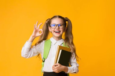 Okula geri dönelim. Gülümseyen İlk Sınıf Schoolgirl Sarı Stüdyo Arka Kamera At Ok Jest Gösteren. Kopyalama Alanı