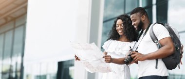 Gündelik giysiler içinde siyah bir çift modern bir binanın önünde duruyor, haritaya bakıyorlar, tahminen günlerini şehri keşfederek geçiriyorlar, uzayı kopyalıyorlar.