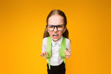 Okul nefreti. Gözlüklü kızgın liseli kız sarı arka plandaki kameraya kükrüyor ve kaşlarını çatıyor. Yüksek Açı Stüdyo Çekimi