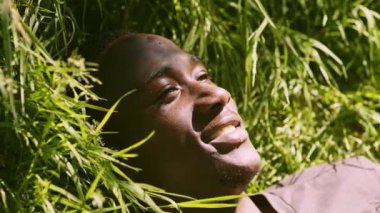 Saf mutluluk. Barışçıl Afrikalı Amerikalı adam yeşil çimlere uzanıp yaz güneşinin tadını çıkarıyor.