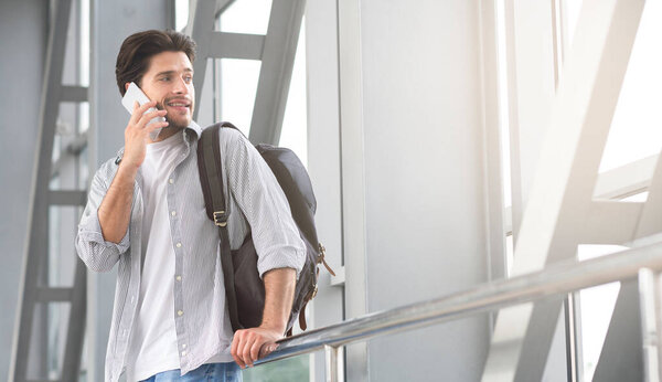 Красивый путешественник разговаривает по мобильному телефону в аэропорту, ждет посадку на рейс, панорама с бесплатным пространством
