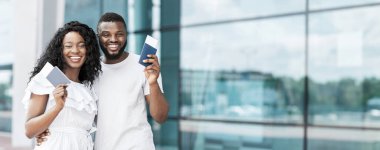 Mutlu, genç siyah bir çift havaalanı penceresinin önünde duruyor. Biletlerini ellerinde tutuyorlar. Bir sonraki yolculuklarının beklentisi içinde.