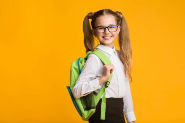 Sevimli İlköğretim Öğrenci Kız Studio Sarı Arka Plan Üzerinde Kamera Bakarak Gülümseyen. Okula geri dönelim. Metin için Boş Alan