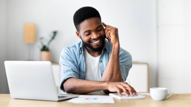 Hoş bir karar. Neşeli Afrikalı iş adamı cep telefonuyla konuşuyor ve programını kontrol ediyor.