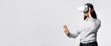 Sanal gerçeklik kulaklığı takan bir kadın elini uzatıyor ve sanal dünyadaki bir şeyle etkileşime giriyor gibi görünüyor..