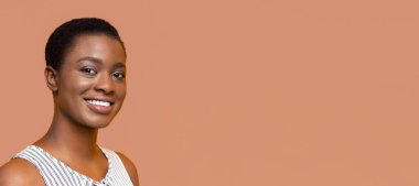 Kısa siyah saçlı Afrikalı Amerikalı genç bir kadın. O, kameraya parlak bir şekilde gülümsüyor ve sıcak, yaklaşılabilir bir ifadeye sahiptir. O, beyaz ve siyah çizgili kolsuz bir gömlek giyiyor.