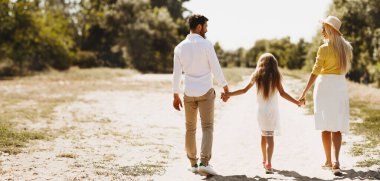 Kırsalda yaz. Karantinadan sonra gezintiye çıkan ve el ele tutuşan üç kişilik aile..