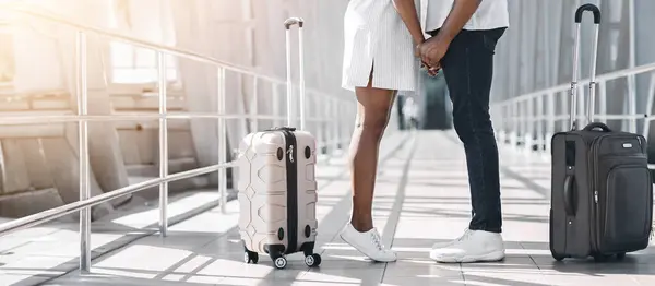 stock image Cropped of black couple stands in an airport terminal holding hands, looking at each other with love. Both are wearing casual clothing and holding suitcases, suggesting they are preparing for a trip