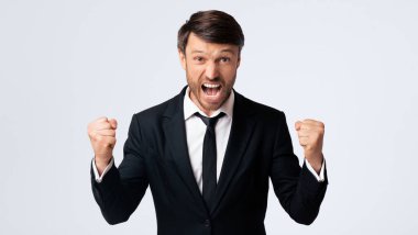 Takım elbiseli, beyaz gömlekli ve siyah kravatlı bir adam beyaz arka planda duruyor, ağzı açık bağırıyor ve yumruklar havada..