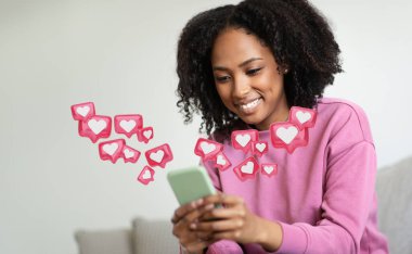 Kıvırcık saçlı genç siyah bir kadın kanepeye oturur ve akıllı bir telefona bakarken gülümser. Etrafı küçük pembe simgelerle çevrili, içinde beyaz kalpler olan..