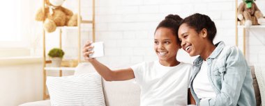 Afrikalı kız kardeşler eğleniyor, akıllı telefon tutuyor, evde selfie çekiyor, boşluğu kopyalıyor.