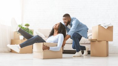 Genç Afro-Amerikan oyuncu, mutlu kadınıyla birlikte paketleme kutusunu itiyor. Yeni eve taşınırken eğleniyor.