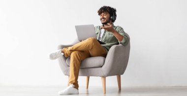 Beyaz stüdyo arka planında oturan yakışıklı Hintli çocuk dizüstü bilgisayar ve kulaklık kullanıyor, arkadaşı ya da sevgilisi ile video görüşmesi yapıyor, kopyalama alanı. Modern teknolojiler ve iletişim