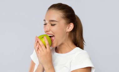 Beyaz Arkaplan 'ın üzerinde duran yeşil elma ısıran genç bayan. Sağlıklı atıştırmalık konsepti. Stüdyo Çekimi, izole edilmiş