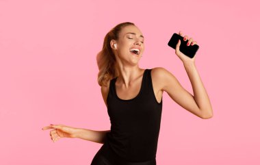 Müzik uygulaması. Kablosuz Kulaklıklı Fit Kız Cep Telefonu Tutuyor Dansçı ve Sarı Stüdyo Arkaplanı Üzerinde Şarkı Dinliyor.