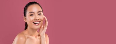 Sensual young beautiful asian lady posing topless on purple studio background, touching her pretty face and smiling, enjoying her silky good-looking healthy skin, copy space, closeup