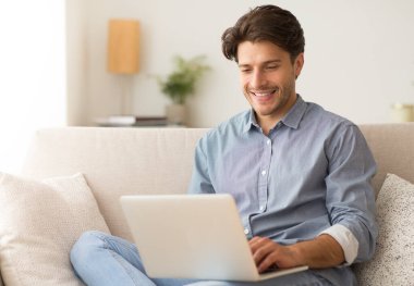 Uzak İş. Evde Kanepede Oturan Laptop Üzerinde Çalışan Adam. Metin için Boş Alan