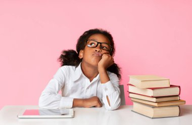 Tablet bilgisayar ve sarı arka planda kitap yığınının arasında oturan sıkıcı siyahi kız. Sıkıcı Ödev Konsepti