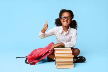 Okulu seviyorum. Afro Schoolgirl Gesturing Thumbs-Up Sarı Arka Plan Üzerinde Studio Kitap Stack Oturan. Boş Alan