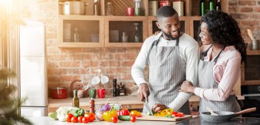 Afro bir aile birlikte yemek pişiriyor, bir kadın kocasına bakıyor, boş bir alan.