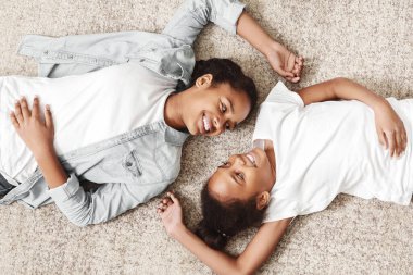 Evde yüz yüze halıüzerinde yatan iki güzel Afrikalı kız kardeş, panorama