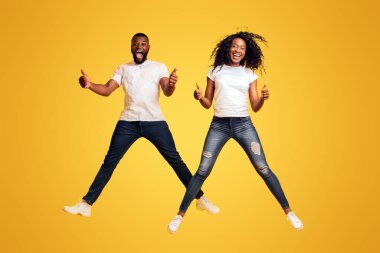 Mutlu Siyah Adam ve Kadın Havada Atlama ve Thumbs Up, sarı arka plan gösteren
