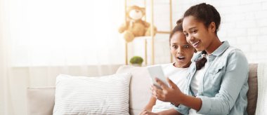 Şok edici mobil uygulama. Afrikalı kız küçük kız kardeşine yeni cep telefonu uygulamasını gösteriyor, evinde oturuyor, kopyalama alanı var.