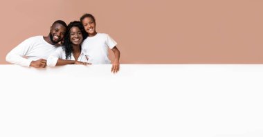 Aileler için teklif et. Gülümseyen Afrikalı Amerikalı anne ve baba ve kızı reklam için boş beyaz tahtaya yaslanıyorlar.