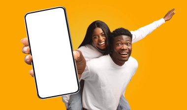 Sarı arka planda duran genç bir Afro-Amerikan çift. Adam önünde akıllı bir telefon tutuyor, ekranı boş..