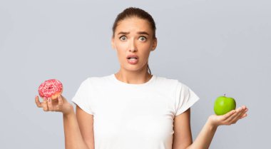 Elma Elması Tutan Kafası Karışık Kadın ve Sağlıklı veya Sağlıksız Yemek Seçen Sağlıklı Olmayan Kadın Beyaz Arkaplanda Oturuyor. Stüdyo Çekimi, Panorama