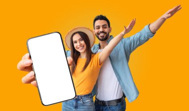 Çok ırklı bir çift, parlak sarı bir arkaplan önünde yan yana durur. Kadın elinde boş ekranlı bir akıllı telefon tutuyor.