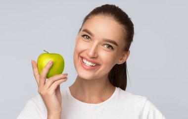 Elma tutan gülümseyen kız beyaz arka planda duran kameraya bakıyor. Stüdyo Çekimi, izole edilmiş