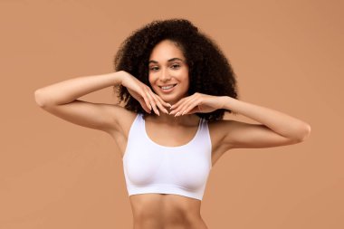 Beyaz gülüşlü ve kıvırcık saçlı Afro-Amerikalı bir kadın, esmer arka planda beyaz bir atlet giyerken bir portre için poz veriyor.