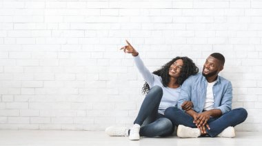 Rüyasında Afrikalı genç bir çift oturma odasında yerde oturuyor, yan bakıyor, kadın boşluğu işaret ediyor.