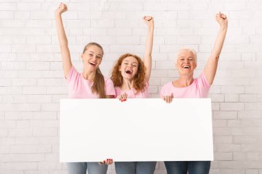 Göğüs kanseri konsepti. Pembe tişörtlü, beyaz tuğla duvarın üzerinde duran boş posterli üç farklı yaşta kadın. Model
