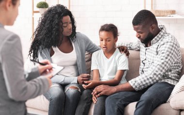 Çocuk Kavramında Bipolar Bozukluk. Küçük Afrikalı Amerikalı kız ve ailesi resepsiyonda, çocuk duygularını doktorla paylaşıyor.