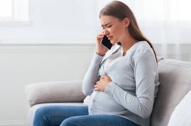 Cep telefonuyla konuşan hamile bir kadın evdeki koltukta oturmaktan acı çeken bir doktoru arıyor..