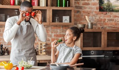 Afro adam ve kızı mutfakta eğleniyor, kız salatalık içinde şarkı söylüyor, baba domates gözlü, boş alan