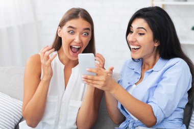 Arkadaşına telefonda mesaj gösteren mutlu kız koltukta oturan bir şey için heyecanlanıyor. Seçici Odaklanma