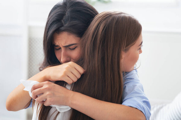 Friendship And Support. Depressed Girl Crying Hugging Her Compassionate Friend Complaining About Problems Sitting On Couch Indoor. Selective Focus